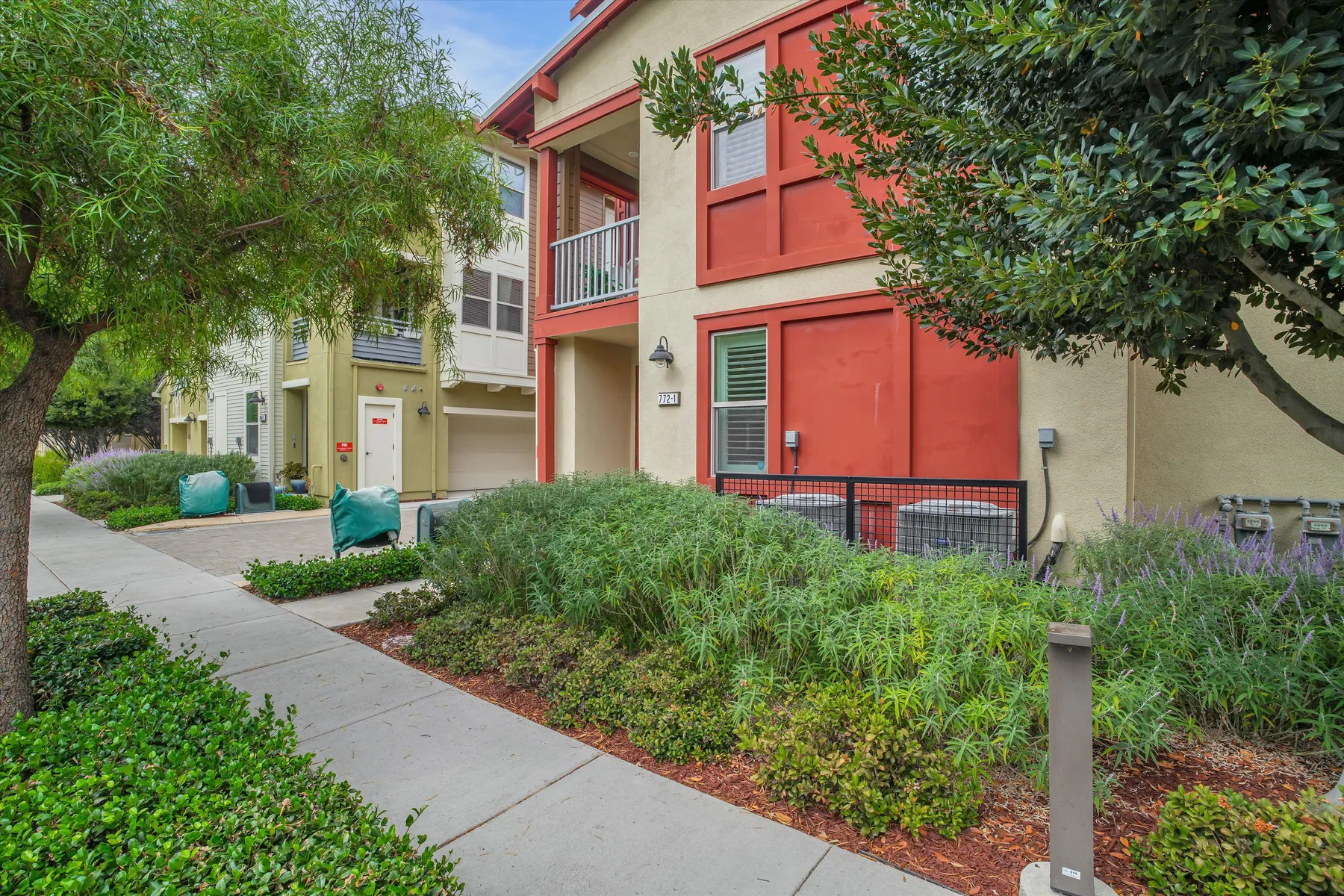 Landscaped sidewalk with shrubs and trees along the red building at Tranquility Circle