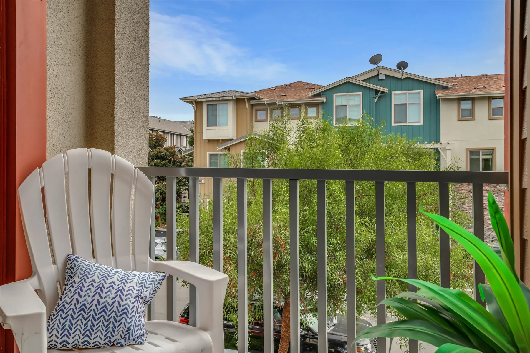 Covered balcony seating framed by red posts, railing and neighboring houses