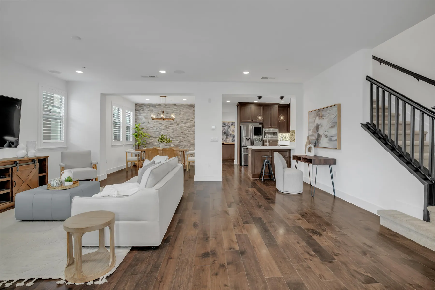 Open living and dining areas with light sofa, wood-look flooring, staircase and stone-textured dining accent wall