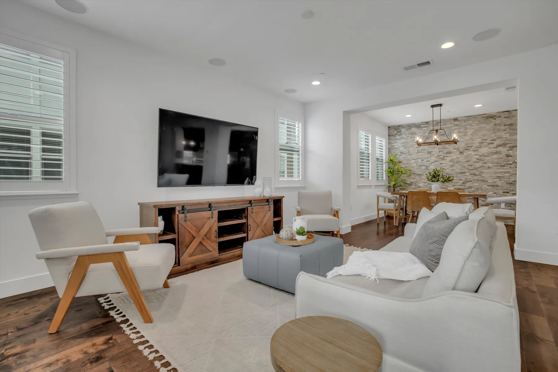 Living room with sofa, wooden lounge chair, wall-mounted television and open dining area
