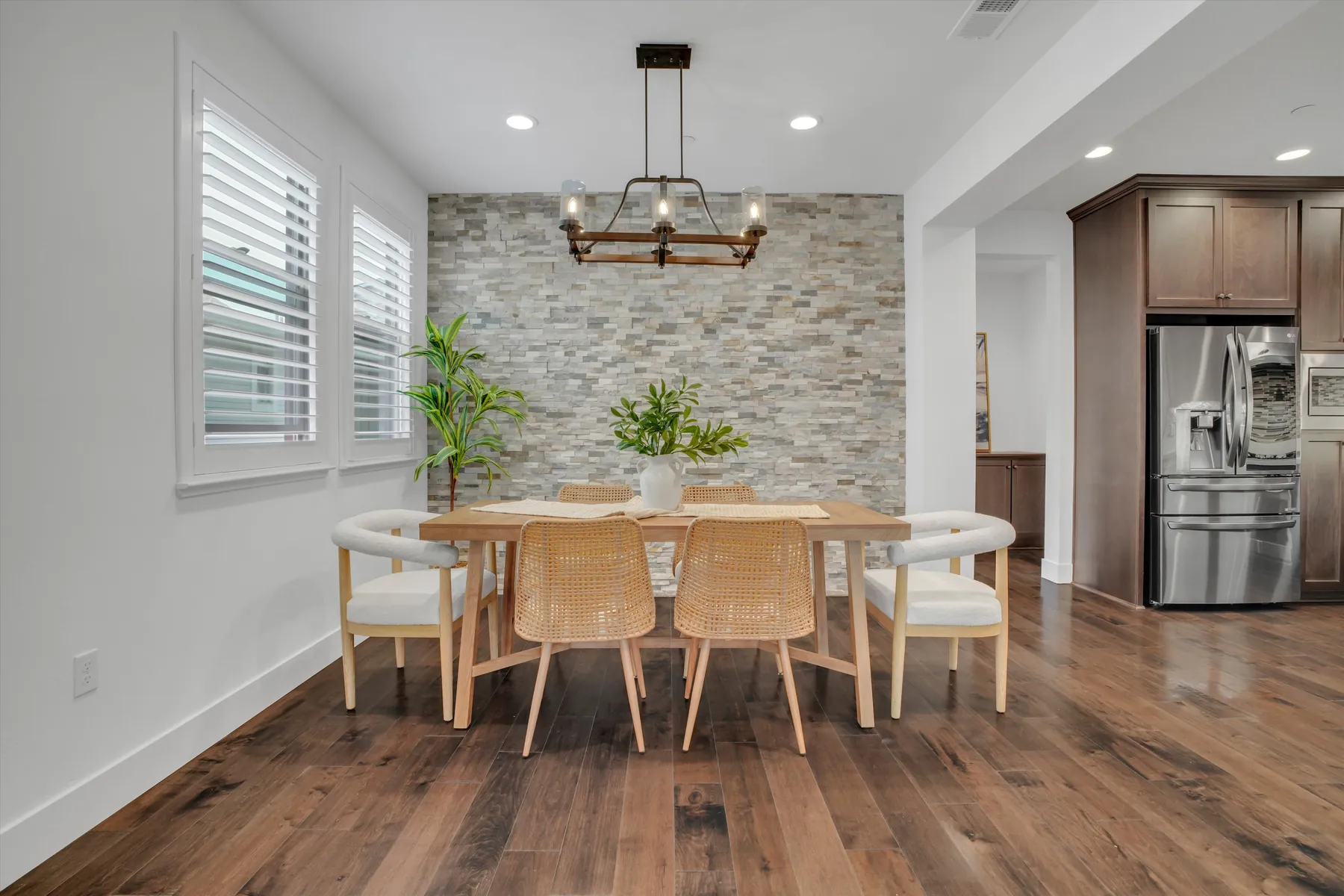 Dining table beside shuttered windows and textured accent wall with the kitchen visible beyond