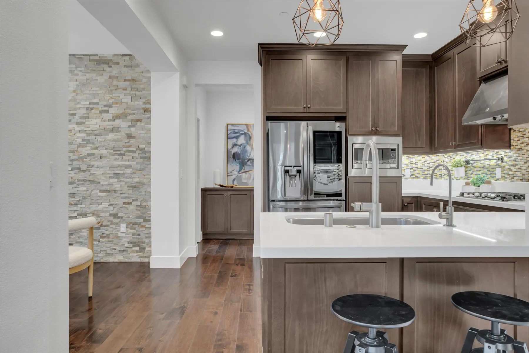 Wide kitchen-island view with sink, pendant lights, stainless refrigerator and dark cabinetry