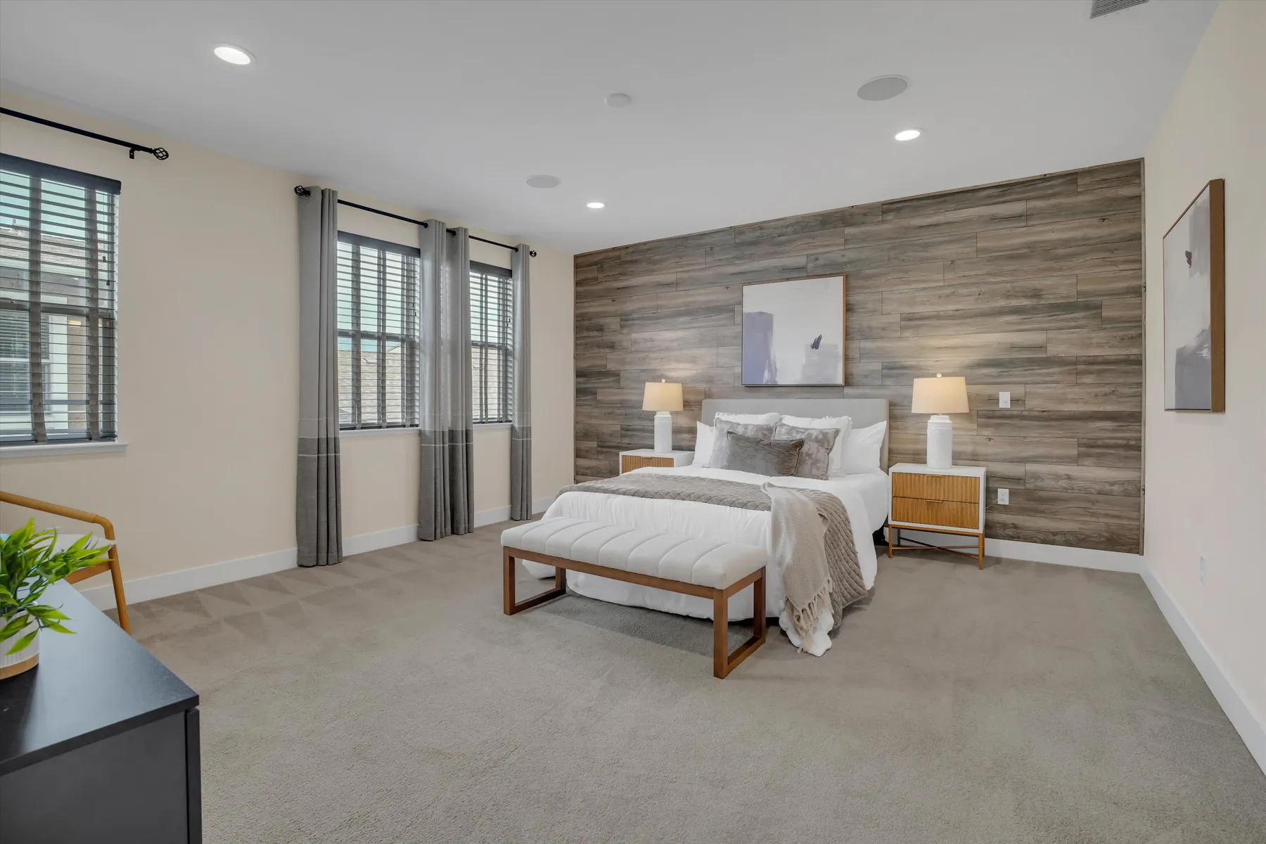 Spacious primary bedroom with wood accent wall, seating area, windows and ceiling fan